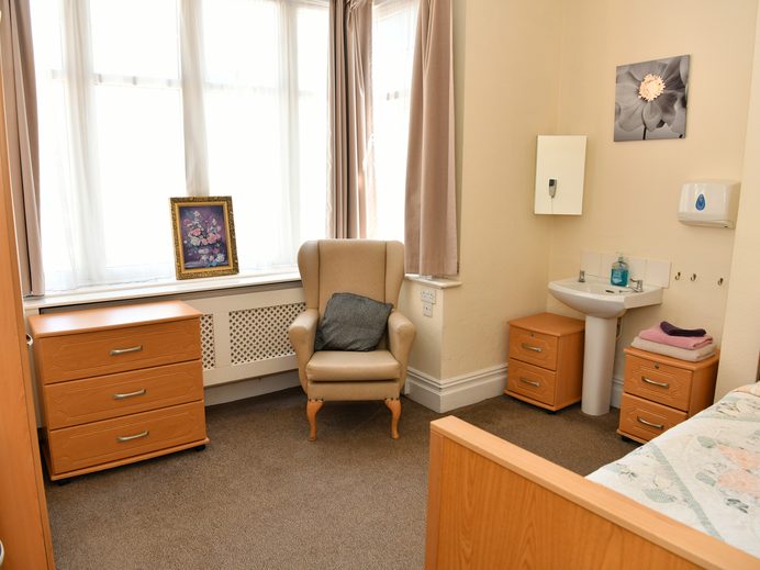 Bright resident's bedroom with armchair and washbasin