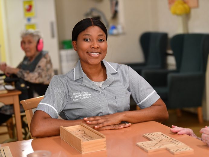 Smiling care assistant playing dominoes in the lounge